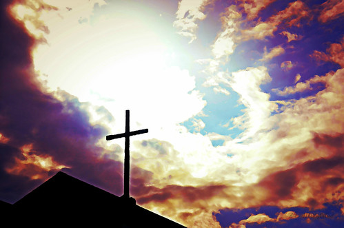 Cross atop a church facing a glorious sky.